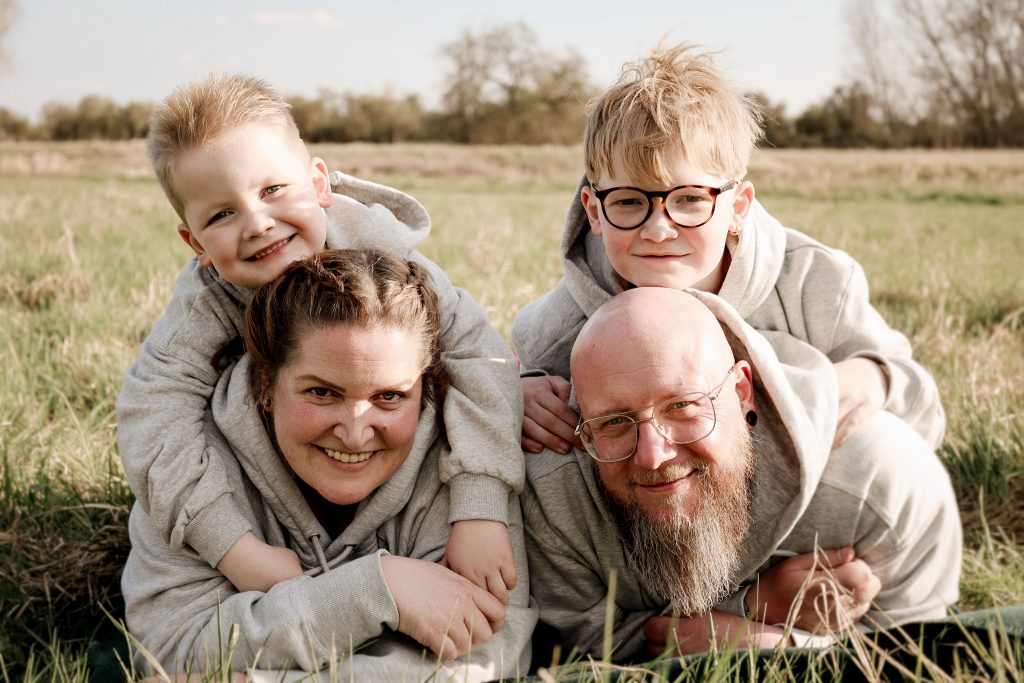 Familie lacht gemeinsam auf einer Wiese während eines entspannten Familienshootings.