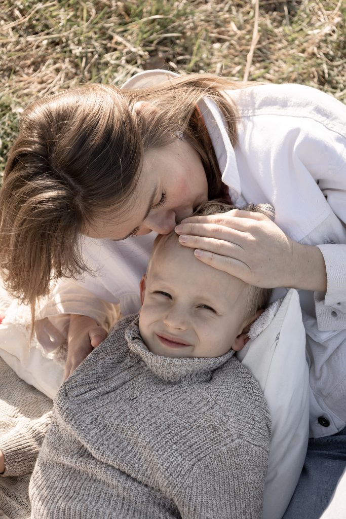 Mutter küsst ihren Sohn bei einem Mama-und-ich-Shooting im Feld liebevoll auf dein Kopf.