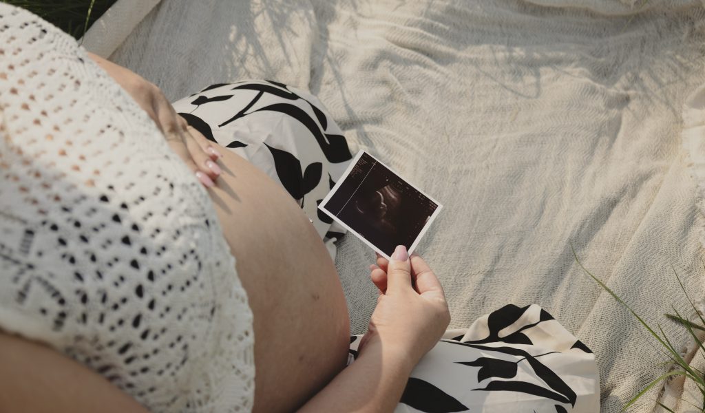 Werdende Mutter hält ein Ultraschallbild bei einem entspannten Babybauch-Shooting in der Hand.