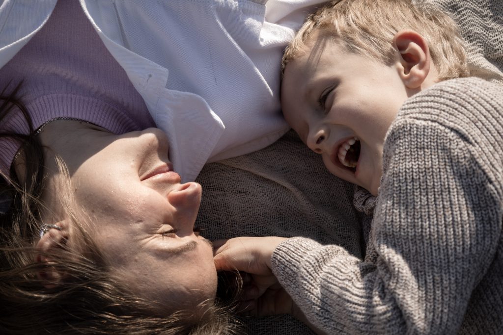 Mutter und Sohn liegen auf einer Decke und lachen bei Mama und ich-Shooting im Abendlicht.